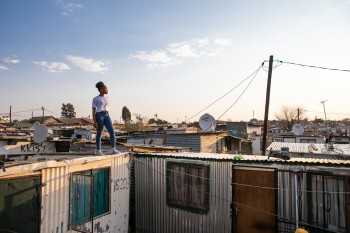 Adolescent girl standing on roof of house in informal settlement