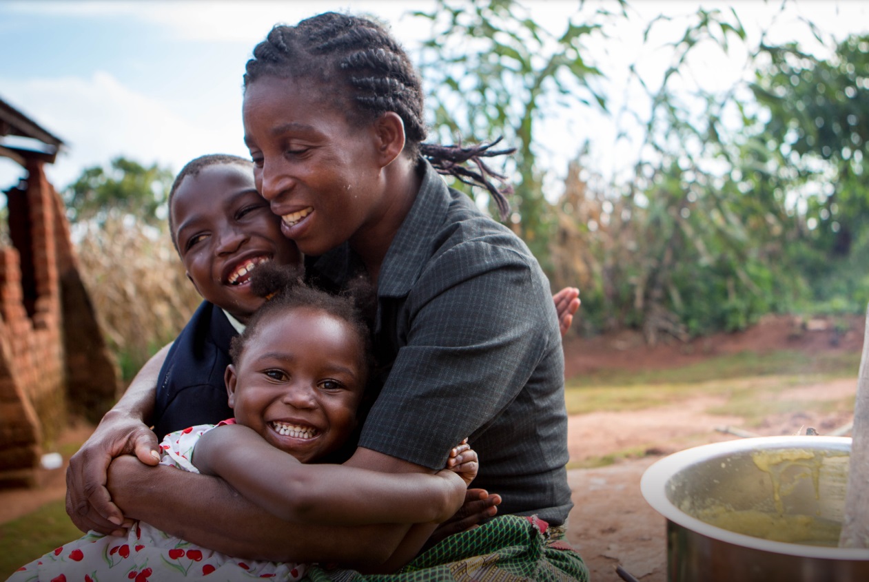 Image shows a mother hugging her children: a small girl and a slightly older boy. All are smiling.