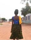 A young woman stands on a dusty street with her back to camera